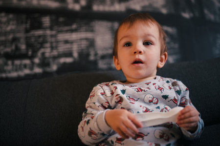 Portrait of cute little toddler sitting on a sofa and watching TVの写真素材