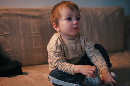 Portrait of cute little toddler sitting on a sofa and watching TVの写真素材