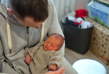 Portrait of father sitting on a sofa and holding newborn baby girlの写真素材