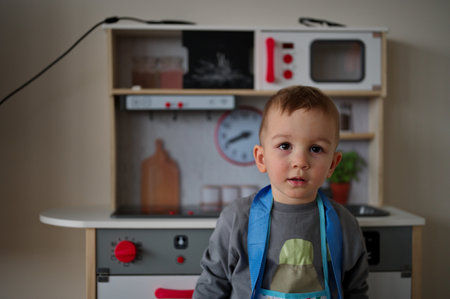 Cute little toddler standing in front of toy kitchen setの写真素材