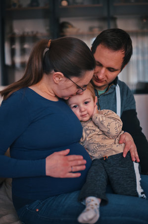 Pregnant mother and her family with little toddler sitting on a sofaの写真素材