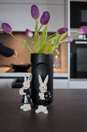 Ceramic Easter bunnies in front of black vase with tulips on kitchen tableの写真素材