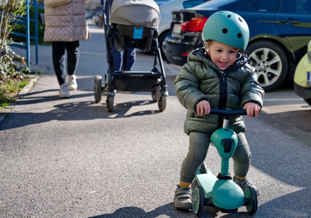 Little toddler on scooter and his parents with baby stroller walking down the streetの写真素材
