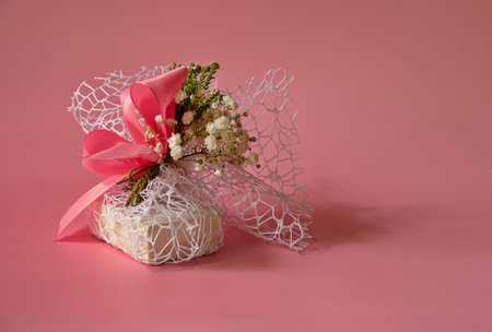 Gift decorated with flowers and bow against pink backgroundの写真素材