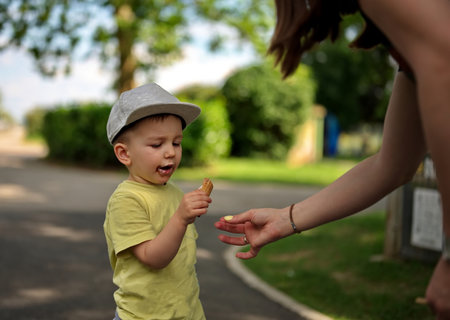 Portrait of little toddler in a park eating ice cream with a help of his motherの写真素材