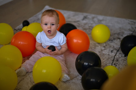 Little baby girl sitting on the floor with balloons around her