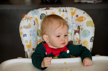 Adorable little baby girl sitting in high chair and eatingの写真素材