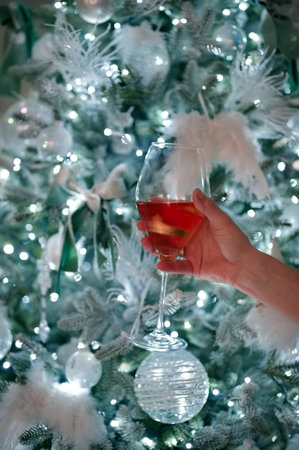 Womans hand holding drinking glass in front of Christmas treeの写真素材