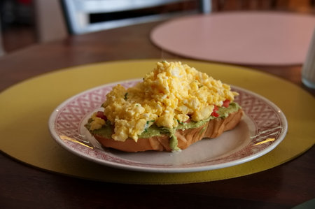 Slice of bread with avocado an scrambled eggs on the kitchen table