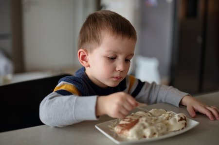 Little boy sitting at the table and eating cakeの写真素材