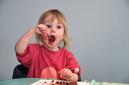 Little girl sitting at the table and eating chocolate cakeの写真素材