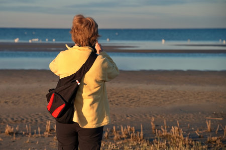 Mature woman standing on the beach and taking photoの写真素材