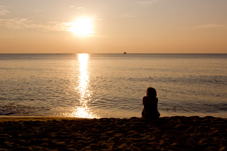 silhouette of a woman sitting on a beach at sunsetの写真素材