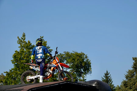 Prague, Czech Republic - September 4 2021: Motocross rider in a blue jumpsuit with a helmet sitting on his motorcycle at the top of the jumping ramp in park Stromovka in Prague. High quality photoのeditorial素材