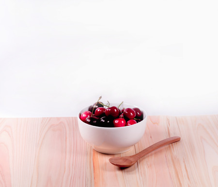 Cherries in white bowl and wooden spoon  on white backgroundの写真素材