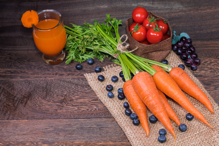 Healthy eating and dieting concept,fresh carrot  and carrot juice or organic healthy juice in glass , tomato ,blueberries on a grey wooden table wall background with copy space .の写真素材