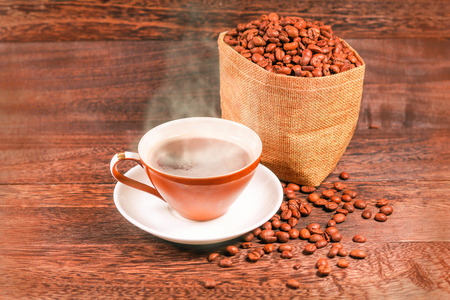 Cup of black coffee and coffee beans in a bag on wooden background with copy space .の写真素材