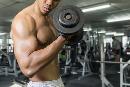 Fitness man in training, showing exercises with dumbbells in gym, soft focusの写真素材