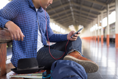 man traveler with backpacker listening to music at trainstation, travel concept