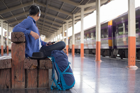 man traveler with backpacker listening to music at trainstation, travel conceptの写真素材