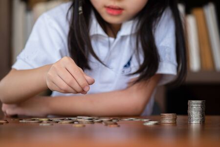 cute girl sitting in library putting money coin to stack on table,saving money conceptの写真素材