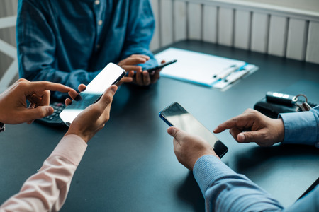 Young business people using smartphone on wooden table share data and send messages in groups,...
