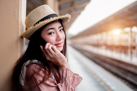 Smiling woman traveler with backpack holding smartphone on holiday relaxation at the train station,relaxation concept, travel conceptの写真素材