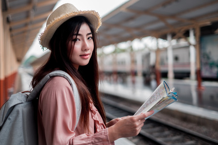 Smiling woman traveler with backpack holding world map planning vacation on holiday relaxation at the train station,relaxation concept, travel conceptの写真素材