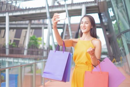 Beautiful women with shopping bags and smartphone enjoying in shopping standing outdoors of shopping mall, shopping conceptの写真素材