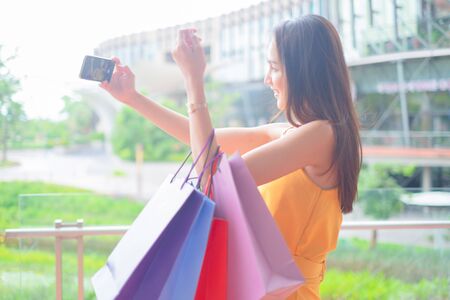 Beautiful women with shopping bags and smartphone enjoying in shopping standing outdoors of shopping mall, shopping conceptの写真素材