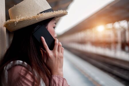 Smiling woman traveler with backpack holding smartphone on holiday relaxation at the train station, relaxation concept, travel conceptの写真素材