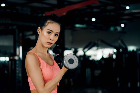 sport woman at fitness gym club doing exercise for arms with dumbbells and showing muscle bodybuilding, fitness concept, sport conceptの写真素材