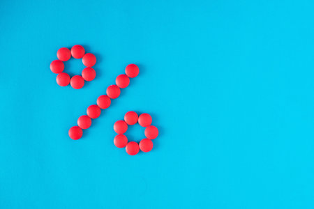 percent sign made from red pills on a blue background. the concept of the cost of medicines and discountsの写真素材