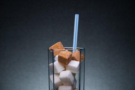 Glass with straw full of sugar and cubes on black background. The concept of prevention of diabetes, the harm of soda, overweight and dietの写真素材