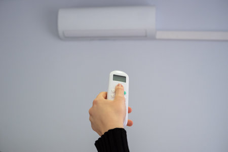 Split air conditioner on a white wall. A woman's hand switches the mode. summer heat.の写真素材