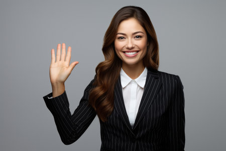 Professional businesswoman in suit waving her hand. Suitable for business communication and networking concepts.の素材