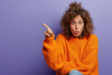 A woman in an orange sweater is pointing to something. She has a surprised look on her faceの素材