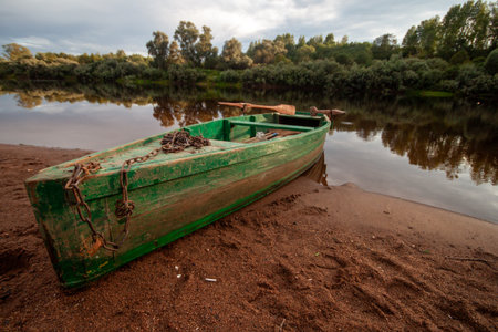A vintage green boat resting on a muddy river bank with trees in the background.の写真素材