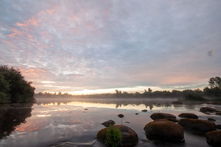 A tranquil lake reflects the colors of a beautiful sunset with mist rising from its surface.