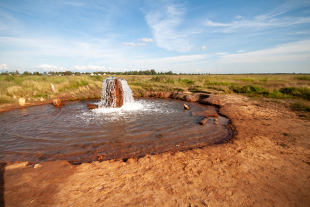 A quaint waterfall situated in a dried up pond area with rocks and dry grassy terrain.の写真素材