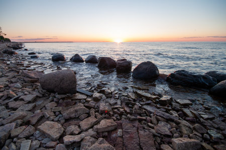 Beautiful landscape at sea with rocks and gentle waves as the sun sets in the distance, creating a warm glow.の写真素材