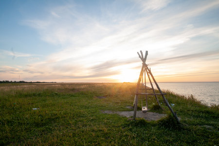 A picturesque scene of a small cabin-like shelter on a grassy bank overlooking a body of water at sunset.の写真素材