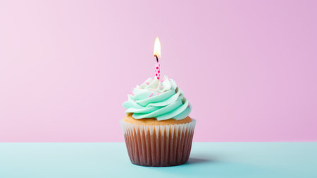 The image features a single cupcake with a lit birthday candle, set against a pastel pink and blue background.の素材