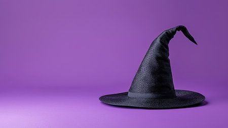 A black witch hat with a purple band lies on a textured purple background, perfect for Halloween-themed decorationsの素材