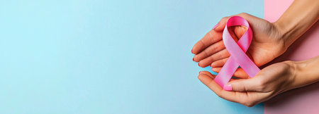 Hands holding a pink ribbon against a pastel background, symbolizing Breast Cancer Awareness Month in October, with ample copy space.の素材