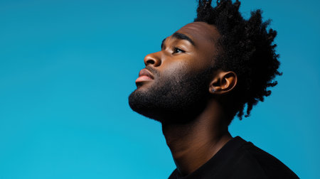 An African American male displays a determined expression in a powerful side profile against a blue background.の素材