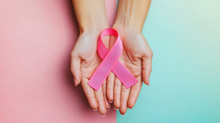 Hands holding a pink ribbon against a pastel background, symbolizing Breast Cancer Awareness Month in October, with ample copy space.の素材