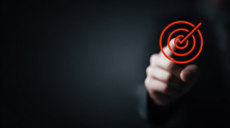 A hand touches a glowing red digital target icon with a white checkmark in the center, set against a dark background, symbolizing successful business goal setting, task completion, and hitting a strategic objective. This image is perfect for presentations, marketing, and articles on strategy, success, and performance.の素材