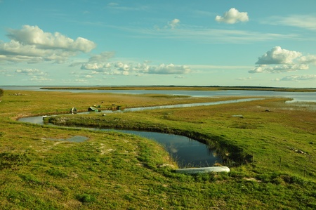 Small boats moored in a waterway inlet in open flat marshland stretching to the horizon.の写真素材