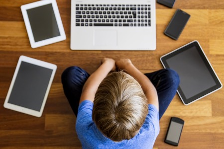 Little boy using tablet sitting on wooden floor. Digital tablets, mobile phones all around. Top view. Education, learning, technology conceptの写真素材